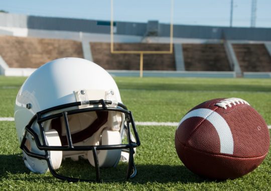 American football and helmet on field with goal post in background.